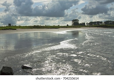 Dutch riverside with sandbank,waves, sunlight and reflection in water, canal floodplain, bushes and trees on horizon, cloud and sunny landscape, river surface, coast with sunlight, back light