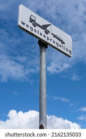 Dutch road sign with icons and text 'Wegsleepregeling' (towing away regulation) on a zinc pole. No parking. Blue sky with clouds. Black text on white - Shutterstock ID 2162135033