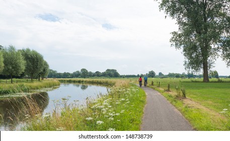 Dutch rural landscape with river and a bike path with a cycling couple.