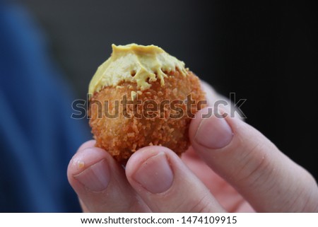 Dutch snack:  Man eating a bitterbal with mustard. Warm stuffed fried meatballs, often served with alcoholic drinks as 