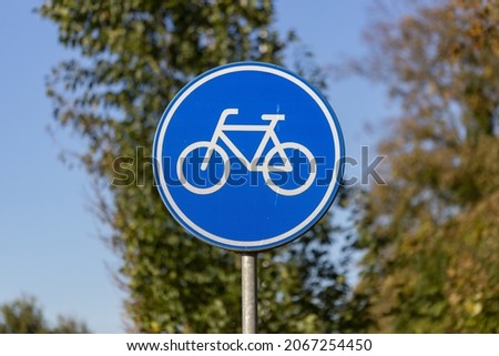 Dutch traffic sign depicting a white bicycle on a blue round metal board meaning there is an obligated bike path for bikeriders against a blue sky