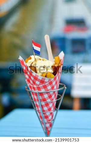 Dutch War Fries  with the Canals of Amsterdam on the background. Typical Dutch street food .Traditional Potato Dish From Netherlands. Fried potatoes   in Paper Cone topped with Mayonnaise