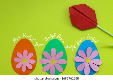 Dutch words Vrolijk Pasen (Happy Easter) with paper eggs, paper flowers and a red paper tulip. On a green background with room for text. 