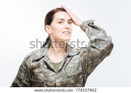 Duty calling. Vigorous optimistic appealing woman  posing in  camouflage uniform and putting her hand on the forehead while  looking at the camera 