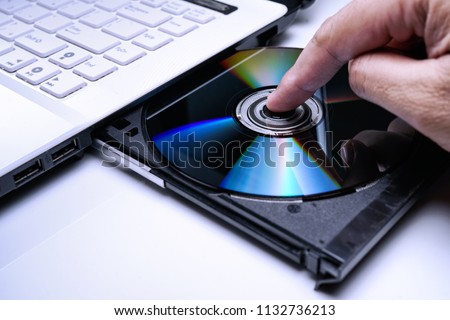 DVD Disk on the white Laptop DVD ROM Tray with a Man Hand. A Piracy conceptual image of burning data into DVD Disk 