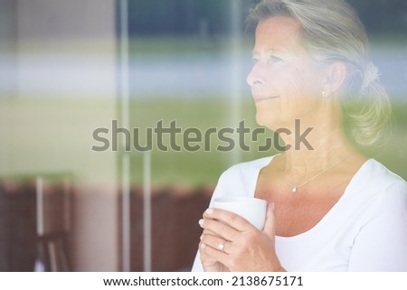 Dwelling on the past. A thoughtful senior woman looking out of her window while enjoying some coffee.
