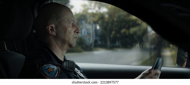 DX Daytime Shot Of Caucasian American Police Officer Patrolling Streets Of Neighborhood In Patrol Vehicle