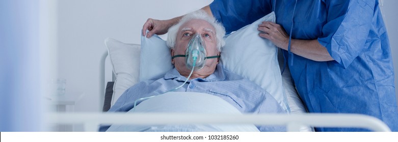 Dying Senior Man With Oxygen Mask And Nurse Caring Of Him In The Health Center