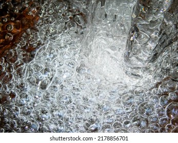 Dynamic Abstract Energy In A Whirl Of Splashing Bubbles At The Base Of A Rock As Water Pours Over Into A Flowing Stream. No People With Copy Space, Shot Outdoors In Natural Light.