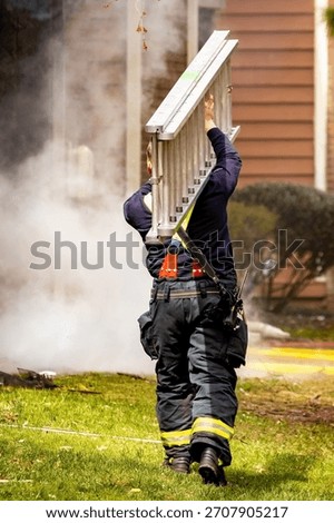 A dynamic, action-oriented view of a firefighter in full protective gear carrying a heavy ladder toward a building engulfed in flames and smoke during a fire emergency