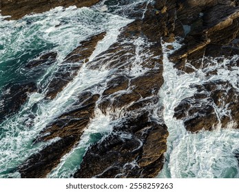 Dynamic aerial view of powerful ocean waves crashing onto the rugged, rocky coastline, surrounded by swirling seafoam, capturing the untamed energy and natural beauty of a scenic seaside environment. - Powered by Shutterstock