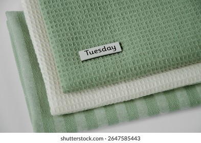 Dynamic angled view of a towel stack with an off-centre ‘Tuesday’ tag, blending texture and typography for contemporary lifestyle or home-organizing visuals