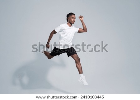 Dynamic black man in sportswear running on grey studio background, in motion shot of motivated young african american male showcasing fitness and active lifestyle, full length, copy space