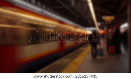 A dynamic, blurred image capturing the motion of a train arriving at a busy station platform at night, with silhouettes of people waiting.