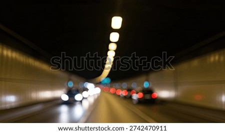 A dynamic, blurred shot capturing the movement of vehicles inside a well-lit tunnel at night. The lights from the cars and the tunnel create streaks of light, emphasizing speed and motion.