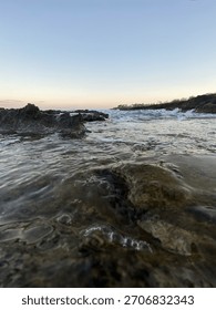 A dynamic close-up seascape capturing powerful ocean waves washing over coastal rocks at golden hour. 