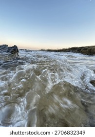 A dynamic close-up seascape capturing powerful ocean waves washing over coastal rocks at golden hour. 