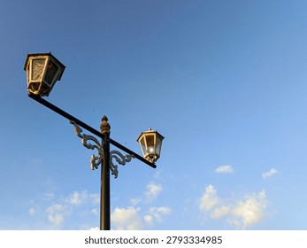 A dynamic diagonal view of an old antique vintage street lamppost with a broken glass panel and a wild bird nest built inside the lamp housing against a blue sky