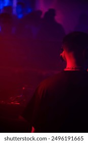 A dynamic and energetic scene featuring DJs mixing music on stage, illuminated by vibrant lights and special effects. The crowd below is a sea of people dancing, enjoying the rhythm.