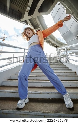 Dynamic full length shot of young woman dancing outdoors in urban area and wearing streetwear