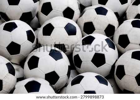 A dynamic, full-frame close-up of multiple black and white soccer balls piled together. The repetitive pentagonal patterns and weathered textures create an intense, energetic, and authentic sporting atmosphere. This high-impact visual style emphasizes team spirit, rigorous training, and readiness for massive global events like FIFA 2026. Ideal for sports retail banners, athletic equipment advertisements, league promotions, and tournament countdown graphics.