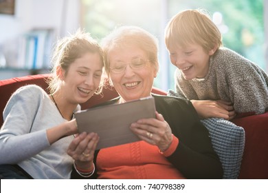 A dynamic grandmother and her two grandchildren having fun with a digital tablet. they're sitting on the couch in the living room. - Powered by Shutterstock