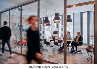 In the dynamic hustle and bustle of a business environment, a group of young business professionals walk down the corridor next to their office, while their colleagues collaborate inside, symbolizing - Powered by Shutterstock