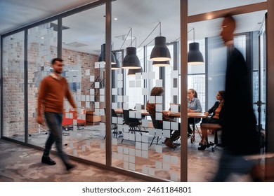 In the dynamic hustle and bustle of a business environment, a group of young business professionals walk down the corridor next to their office, while their colleagues collaborate inside, symbolizing - Powered by Shutterstock