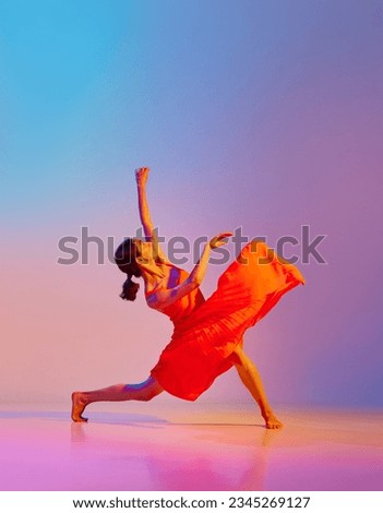 Dynamic image of artistic young woman dancing in elegant red dress against gradient multicolor background in neon light. Concept of modern dance style, hobby, art, performance, lifestyle, ad