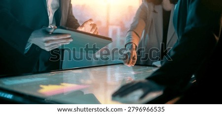Dynamic image capturing a team of professionals collaborating over a large interactive digital touchscreen table and a tablet, set against a backdrop of a modern, sunlit office. The scene exudes innovation, teamwork, and the cutting-edge nature of technology-driven business solutions, perfect for illustrating concepts such as digital transformation, corporate strategy, and creative ideation in the workplace.