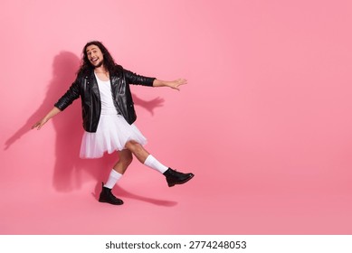 Dynamic image of a cheerful, nonbinary man in a white top, black leather jacket, pink tutu, and crown mid-jump against a pink background. 