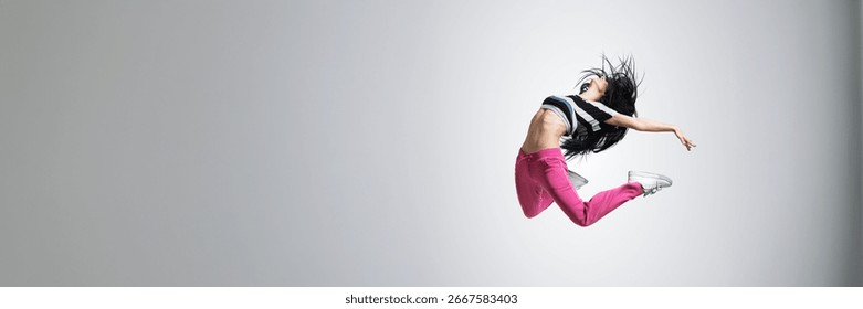Dynamic image of a dancer leaping mid-air, wearing vibrant clothes. Monochrome background with copy space. Ideal for dance, movement, and fitness ads.