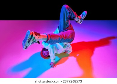 Dynamic image of man in his 30s in motion, dancing breakdance isolated over black studio background in neon light. Concept of contemporary dance, street style, fashion, hobby, youth. Ad