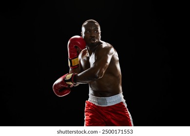 Dynamic image of serious African-American man, boxer with muscular boy, in red gloves and short punching, training isolated on black background. Concept of sport, active lifestyle, body, strength - Powered by Shutterstock