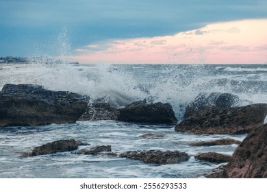 A dynamic image showcasing waves violently crashing against rocks under sunset contrast sky. this vivid depiction highlights natural forces and coastal terrain