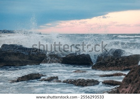 A dynamic image showcasing waves violently crashing against rocks under sunset contrast sky. this vivid depiction highlights natural forces and coastal terrain
