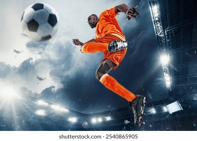 Imagen dinámica del jugador de fútbol con uniforme naranja brillante, saltando al aire, enfocado en el balón durante el momento intenso durante el juego. Partido al aire libre por la noche. Concepto de deporte, torneo, competición, juego