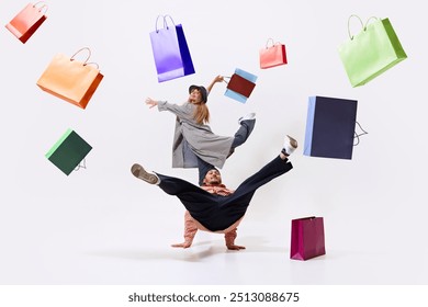 Dynamic image of two young stylish man and woman in ,motion, dancing with many colorful shopping bags flying around, isolated on white background. Concept of shopping, sales, Black Friday, fashion - Powered by Shutterstock