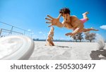 Dynamic image of young focused man catching flying disk and falling down. Friends playing frisbee game on sandy beach by the river. Concept of sport, summer activity, leisure games, friendship