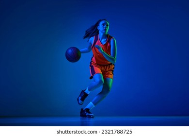 Dynamic image of young girl, basketball player in uniform in motion, playing over blue studio background in neon light. Concept of professional sport, action and motion, game, competition, hobby, ad - Powered by Shutterstock