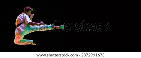 Dynamic image of young man, karate athlete in motions, training over black studio background in neon lights. Concept of martial arts, combat sport, energy, strength, health. Banner. Copy space for ad