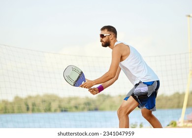 Dynamic image of young man playing beach, paddle tennis, hitting ball with racket. Outdoor training on warm summer day. Concept of sport, leisure time, active lifestyle, hobby, game, summertime, ad - Powered by Shutterstock
