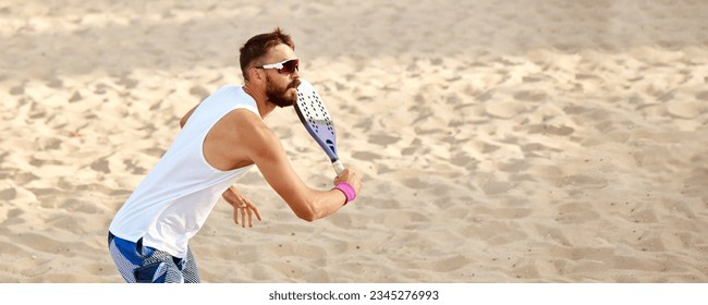 Dynamic image of young man playing beach tennis, hitting ball with racket. Outdoor training on warm summer day. Top view. Concept of sport, leisure time, active lifestyle, hobby, game, summertime, ad