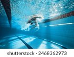 Dynamic image of young man, swimmer in motion, swimming freestyle stroke in pool, training. Concept of professional sport, health, endurance, strength, active lifestyle