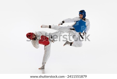 Dynamic image of young men, taekwondo athletes in kimono and helmets training isolated over white background. Concept of martial arts, combat sport, competition, action, strength, education