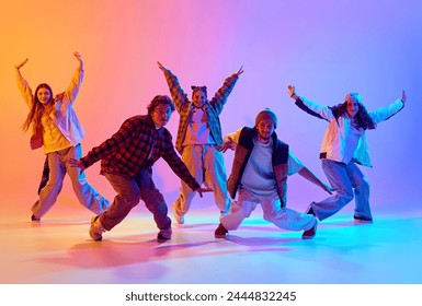 Dynamic image of young people, men and women in casual clothes dancing contemp against gradient studio background in neon light. Concept of modern dance style, hobby, active lifestyle, youth culture