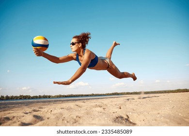 Dynamic image of young woman in motion, playing beach volleyball, hitting ball and falling down on sand. Sunny warm day. Concept of sport, active and healthy lifestyle, hobby, summertime, ad - Powered by Shutterstock