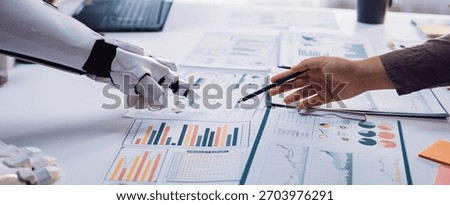 A dynamic interaction between human and robot in a modern office setting, showcasing collaboration on data analysis charts and graphs, emphasizing innovation.Noogenesis