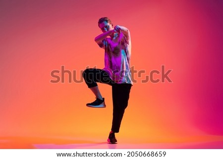 Dynamic lifestyle. One active young man hip-hop dancer training isolated over gradient pink background in neon light. Concept of dance, youth, hobby, dynamics, movement, action, ad