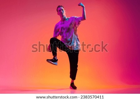 Dynamic lifestyle. One energetic young man hip-hop dancer training isolated over gradient pink background in neon light. Concept of dance, youth, hobby, dynamics, movement, action, ad